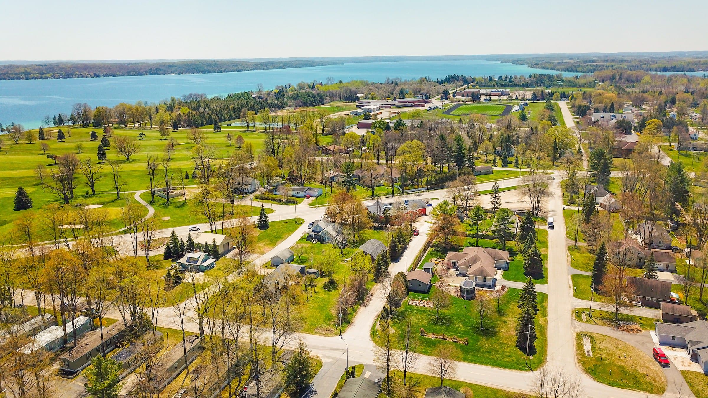 Aerial of Vacation Village's wooded streets alongside the Elk Rapids golf course, with the water beyond