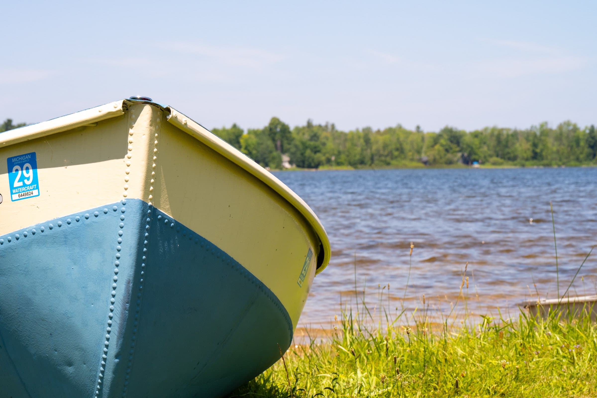 The bow of a yellow and blue canoe resting in the grass at the edge of Bass Lake