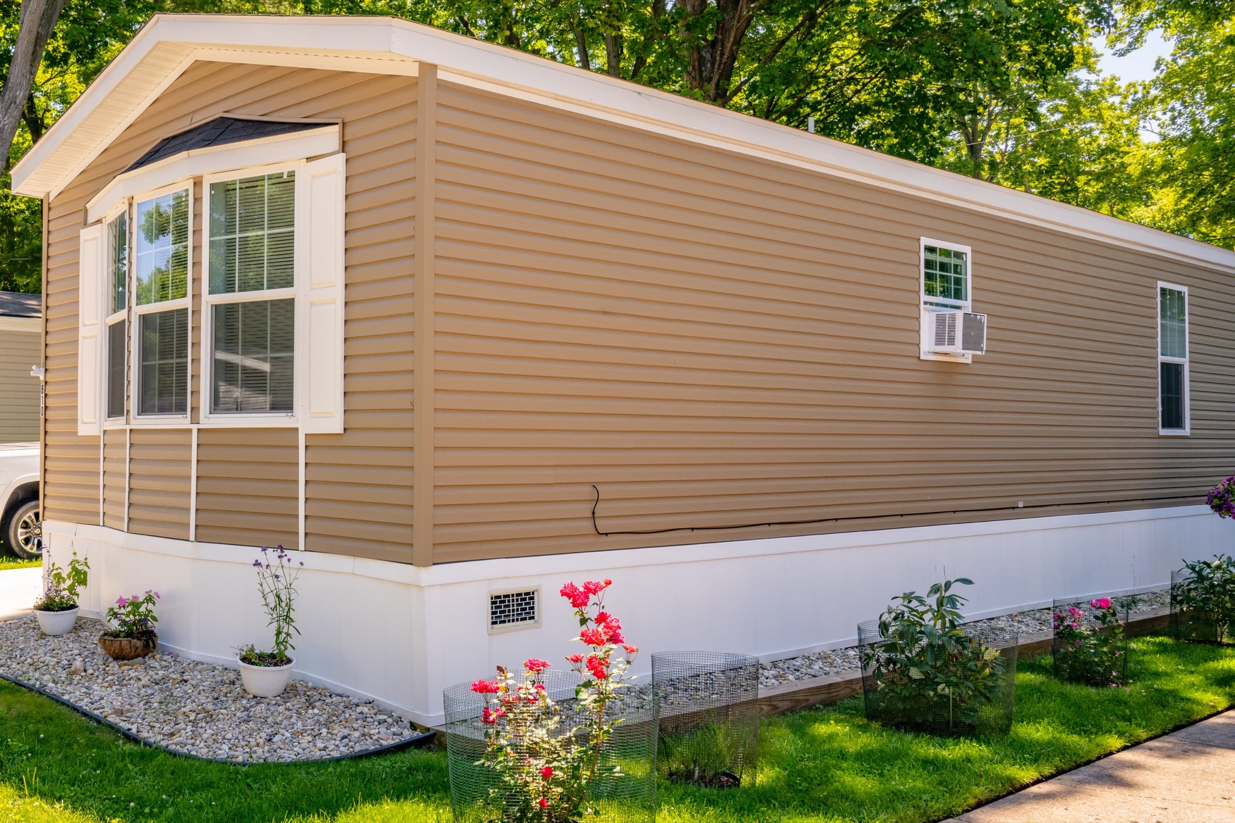 A well-kept manufactured home with roses in bloom along its gravel border