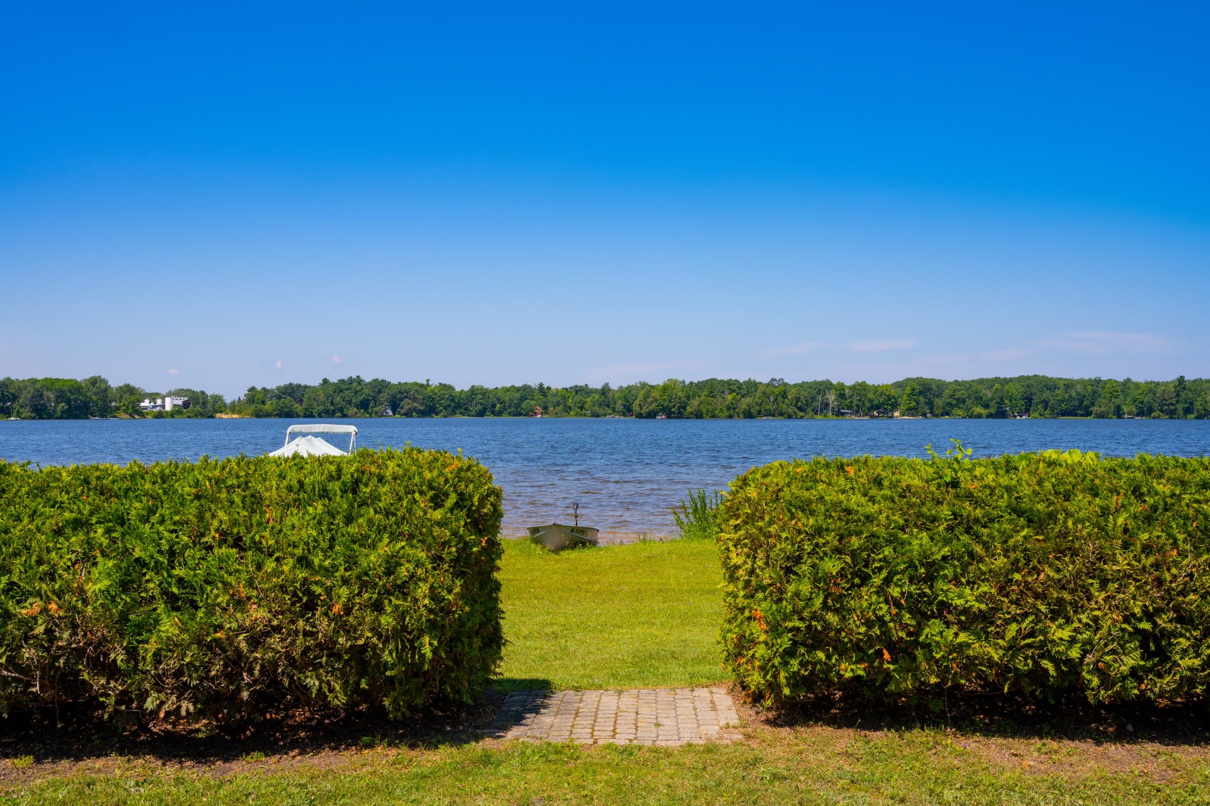 A mown lawn and clipped hedges opening onto Bass Lake, a paver path leading down to the water