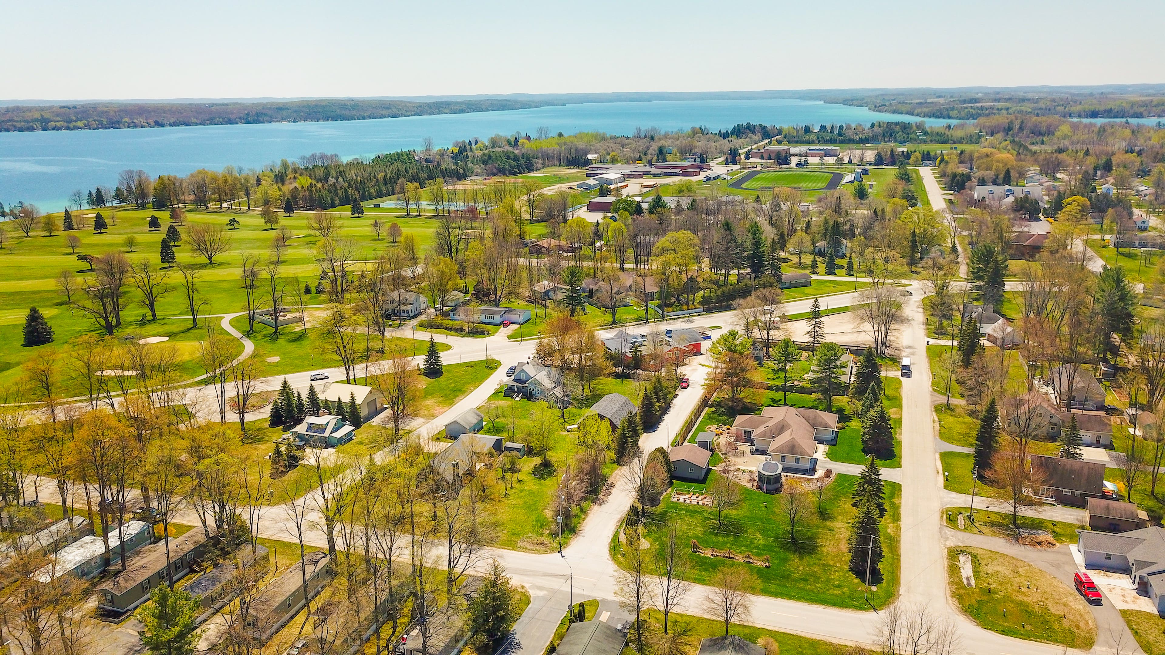 Aerial view over Vacation Village's wooded streets and the golf course, with Bass Lake frontage beyond
